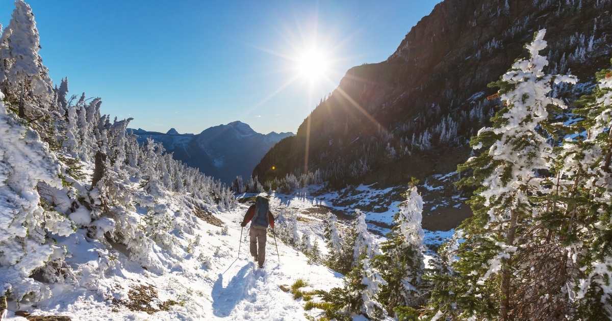 hiker on a snow-covered winter trail with mountains in the background