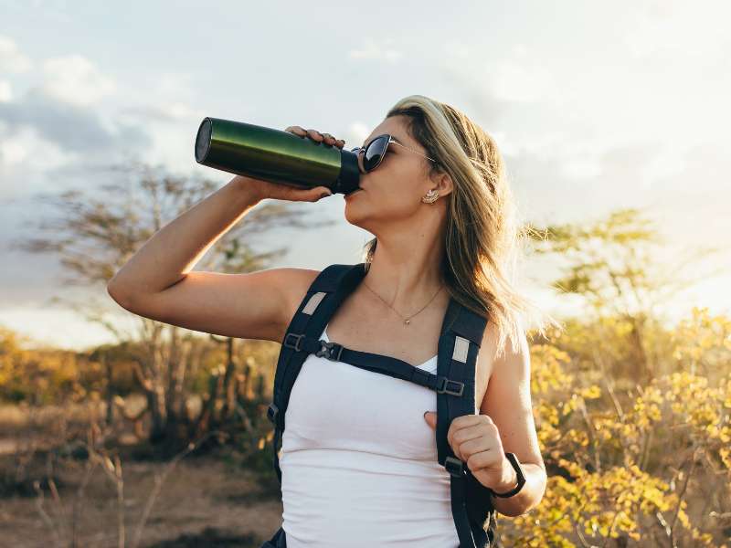 woman drinks water from a water bottle after hiking