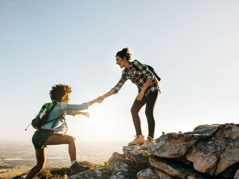 hiking women offering a hand to reach the mountain