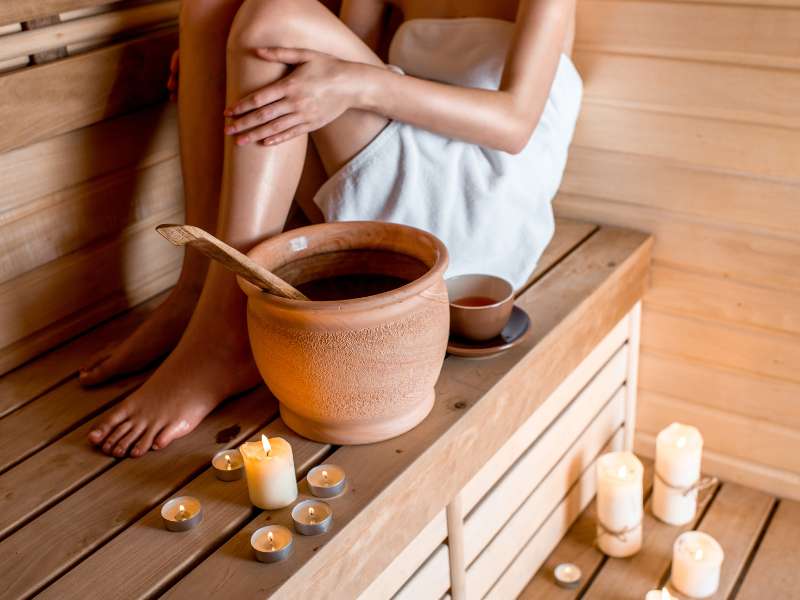 woman sitting in a sauna with candles and jug